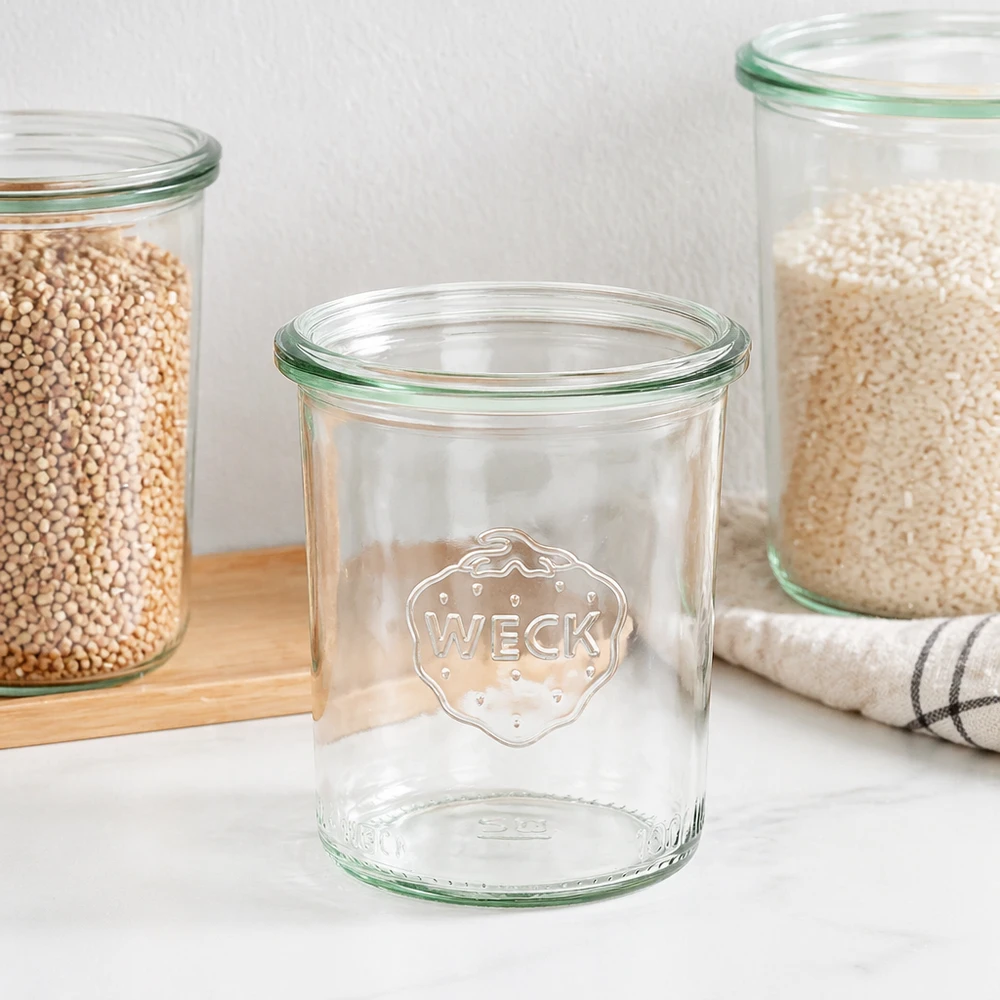 WECK Sturzglas 160ml RR60 mit grünem Rand und Logo, leeres Einmachglas neben gefüllten Vorratsgläsern auf Holzbrett